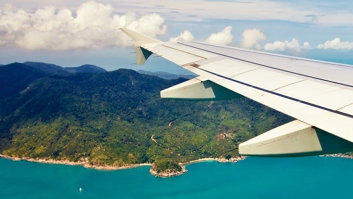 Airplane wing tip over ocean and island featured shutterstock 137460476