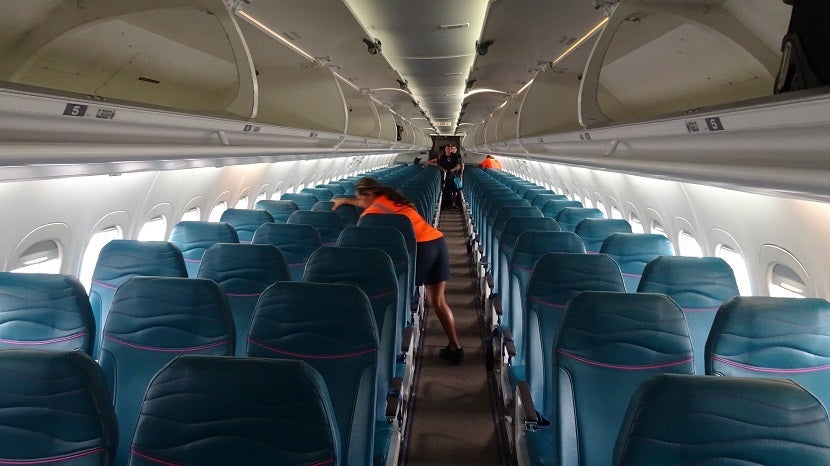 A crew member cleans the cabin of the B717, with seats in a 2-3 configuration.