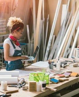 Female artist in her studio standing and looking at her laptop.