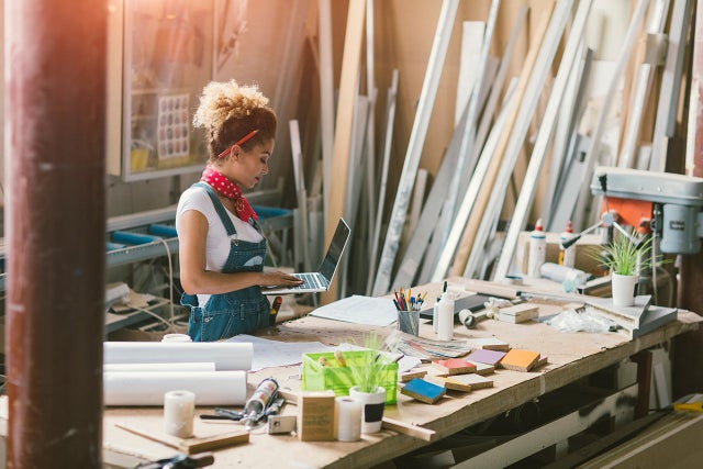 Female artist in her studio standing and looking at her laptop.