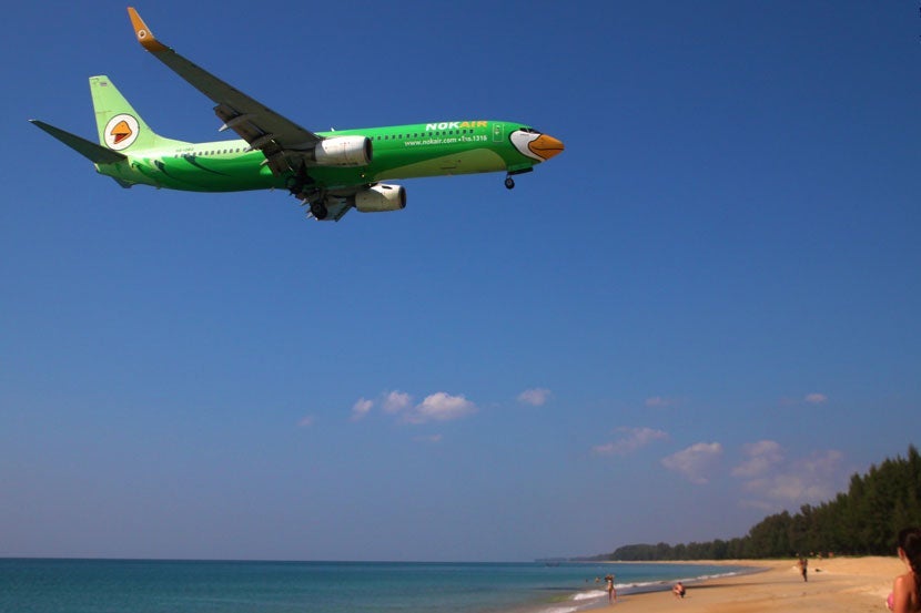 The beach along Phuket Airport's western runway offers an ideal place to stop and watch planes land from the shoreline. Image courtesy Ben Reeves via <a href="https://www.flickr.com/photos/chindit76/16222844438/in/photolist-pXDnAX-qeUHua-q48VC1-qcNy8y-qf5Qkt-Rn7NPB-pXwQN7-4cyS8G-qf5Q72-5uT9rF-pijUGe-pi6yuC-R9GdZt-nXeFpF-qXReG5-qZZpuD-qHzTfb-5uTcyz-5uXtAU-4cySCs-pWUxAk-ASLUn-5uTgYP-5uTaSz-5uTiCz-Rkih1x-Q3R9Y1-Q6DnBx-RkigtR-Q3RahN-qHymJS-qHyjss-5uTjPZ-5uTenZ-ASLVR-R9Ge2T-R9Ge9r-ASLSS-ASG4c-L7EwdK-qZZonZ-qHyE9b-qHyzMq-qHHo8p-qHzBnj-qHHaU6-mQGCW" target="_blank">Flickr</a>.