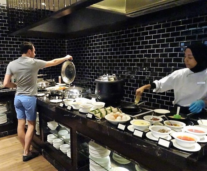 A guest peruses the breakfast buffet while a chef prepares fresh omelettes.