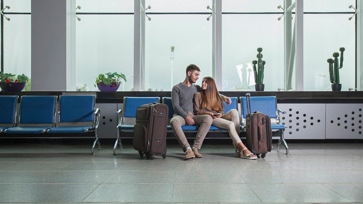 Young couple with luggage sitting on chairs at airport