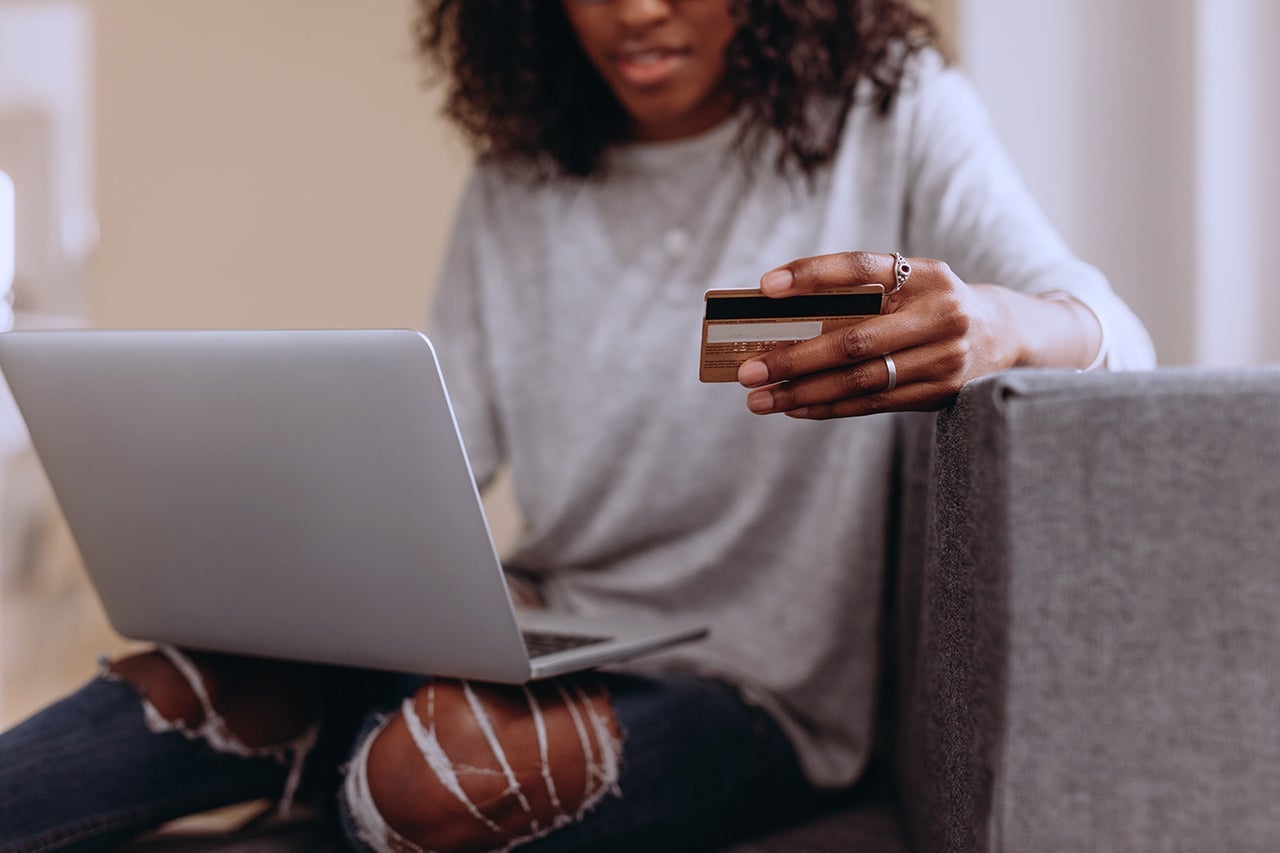 a woman types on her computer while holding a credit card