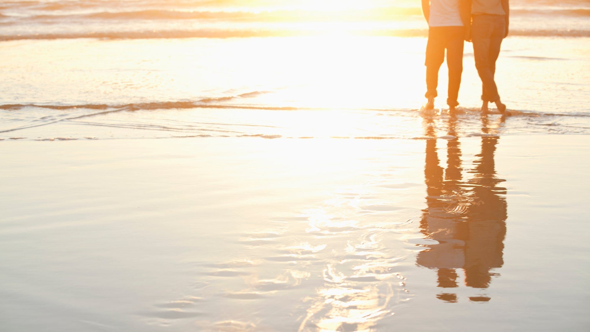 Rear view of a couple standing together on beach at sunset