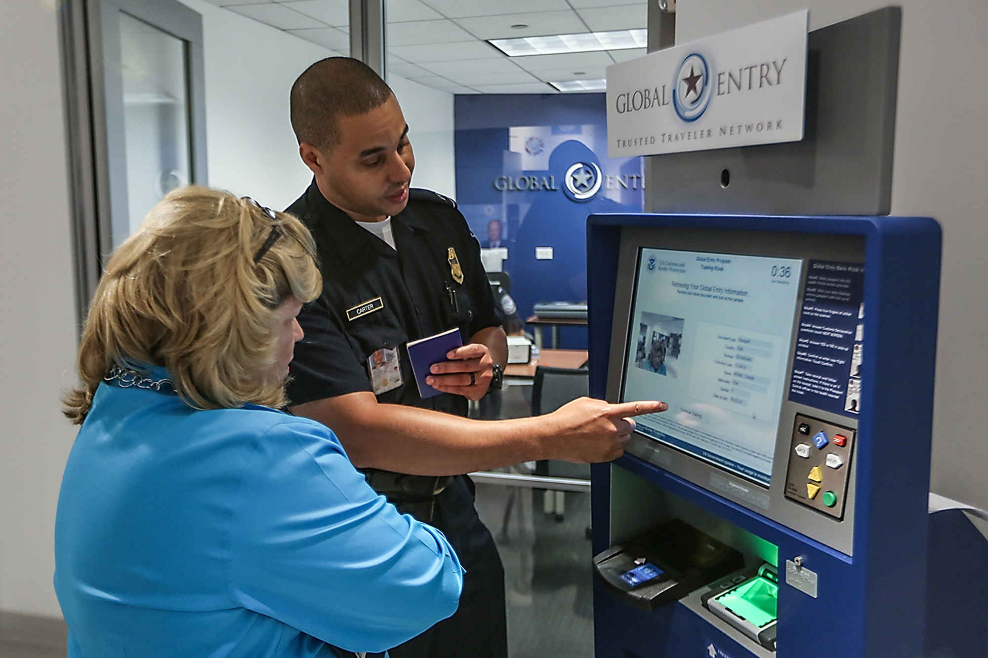 a passport control officer shows someone how to use a Global Entry kiosk