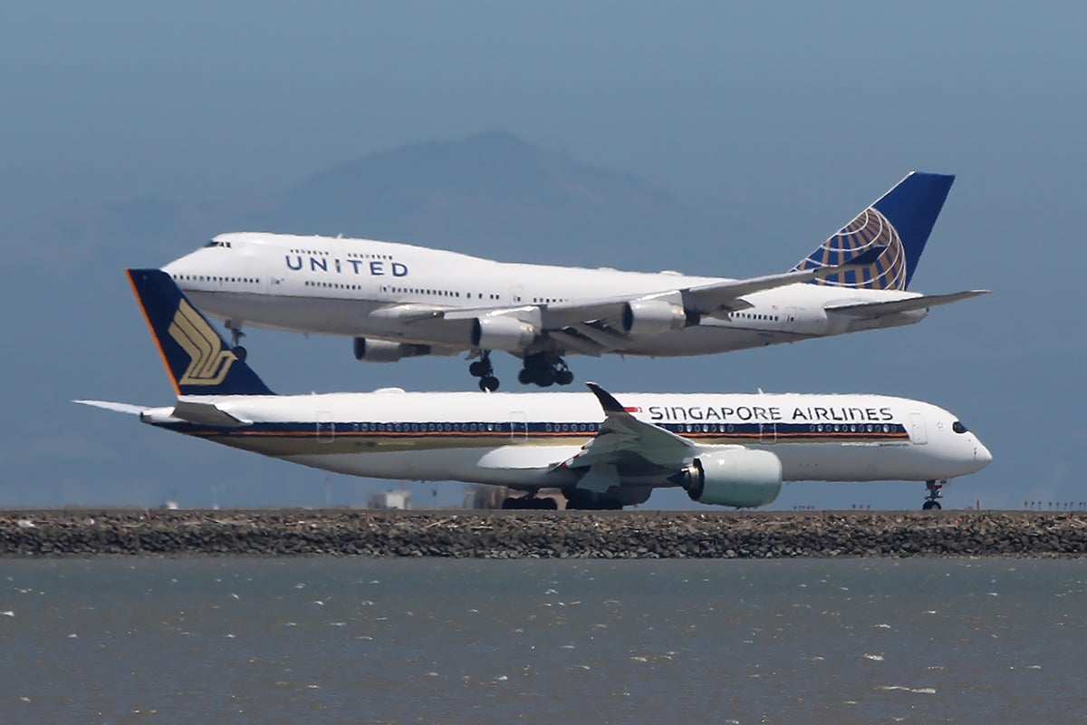 A United 747-400 lands while a Singapore Airlines A350 taxies to takeoff.