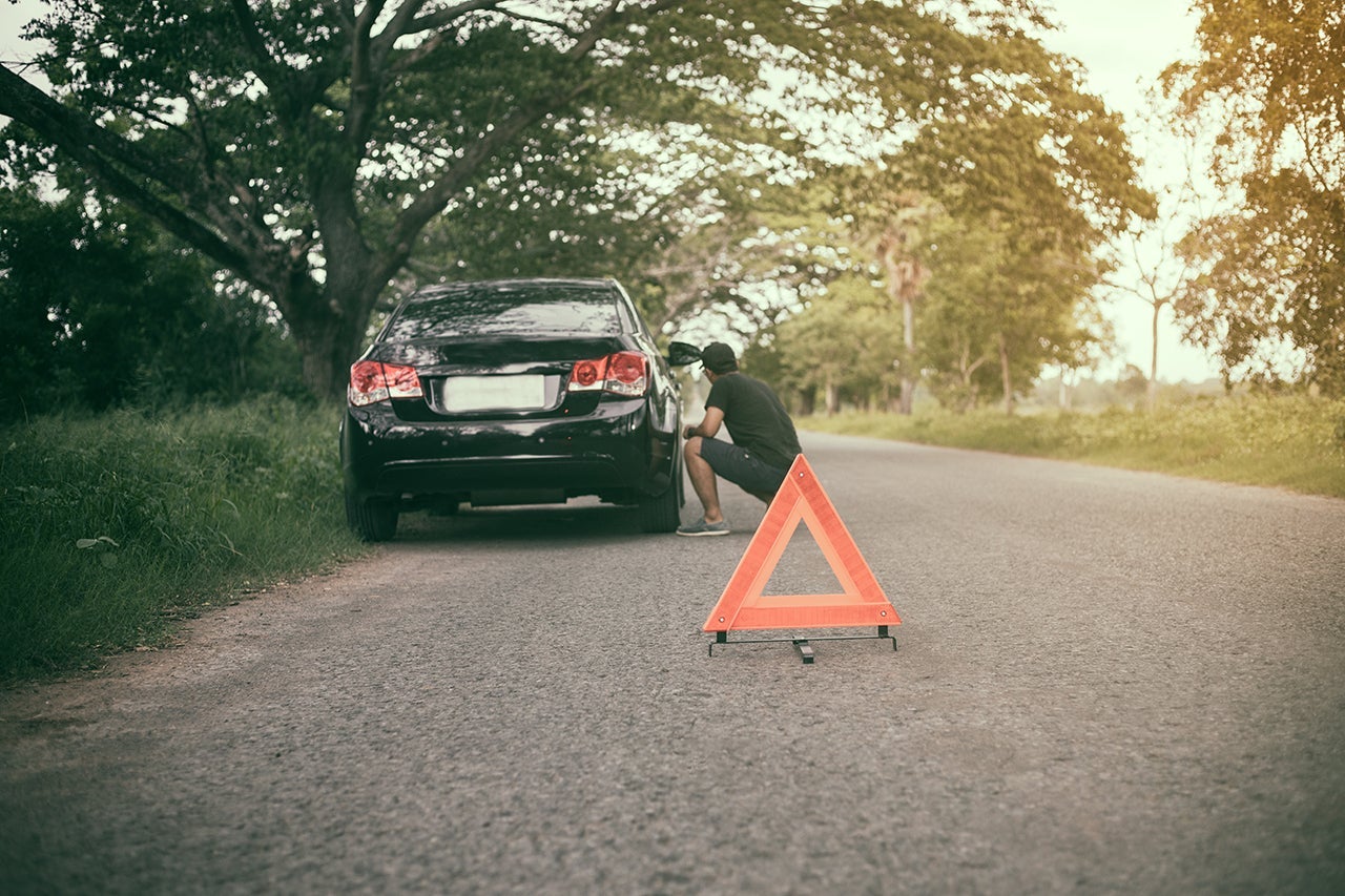 Stressed man sitting after a car breakdown with Red triangle of a car on the road