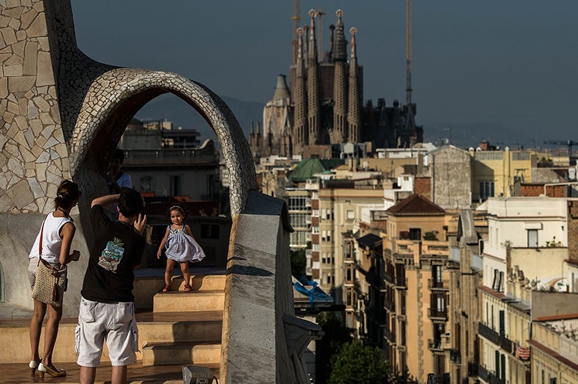 BARCELONA, SPAIN - JULY 24: A couple take pictures of their daughter at the roof of the building 'La Pedrera' or 'Casa Mila' of Antoni Gaudi with La Sagrada Familia on the background on July 24, 2013 in Barcelona, Spain. Foreign visitors to Spain set a new record high in June surpassing six million tourists for the first time ever and climbing by 5.3 percent since June 2012. (Photo by David Ramos/Getty Images)