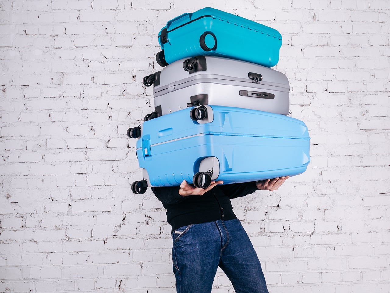 Man holding three heavy suitcases in hand. Travel light. Man holding three heavy suitcases in hand. Travel light. (Photo by ULU_BIRD/Getty Images)