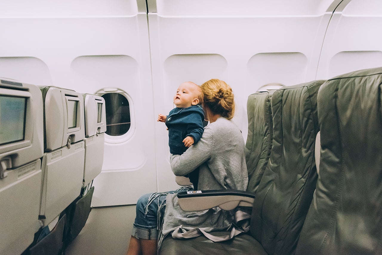 Woman traveling with her baby sitting in an airplane cabin. (Photo by Juanmonino/Getty Images)