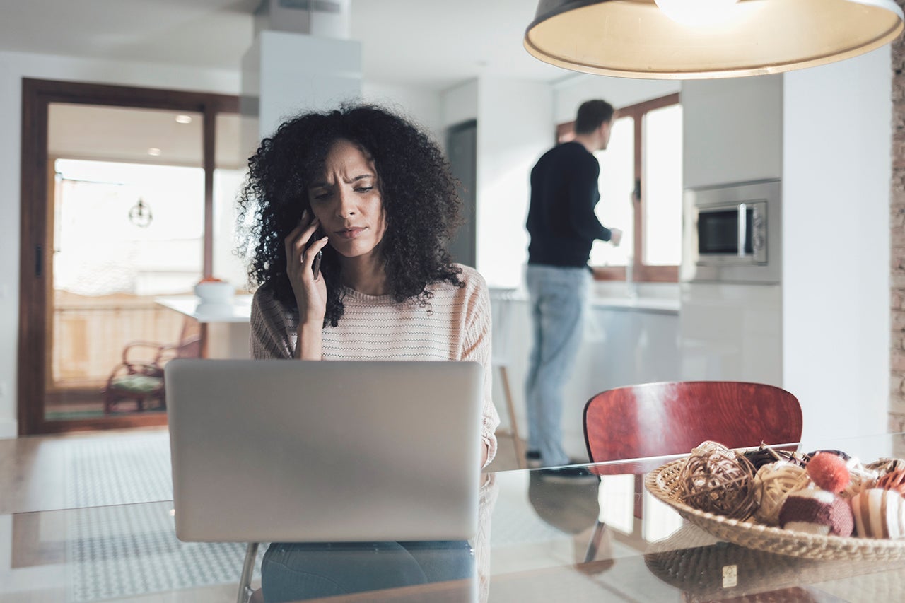 a woman sits at a laptop while making a phone call