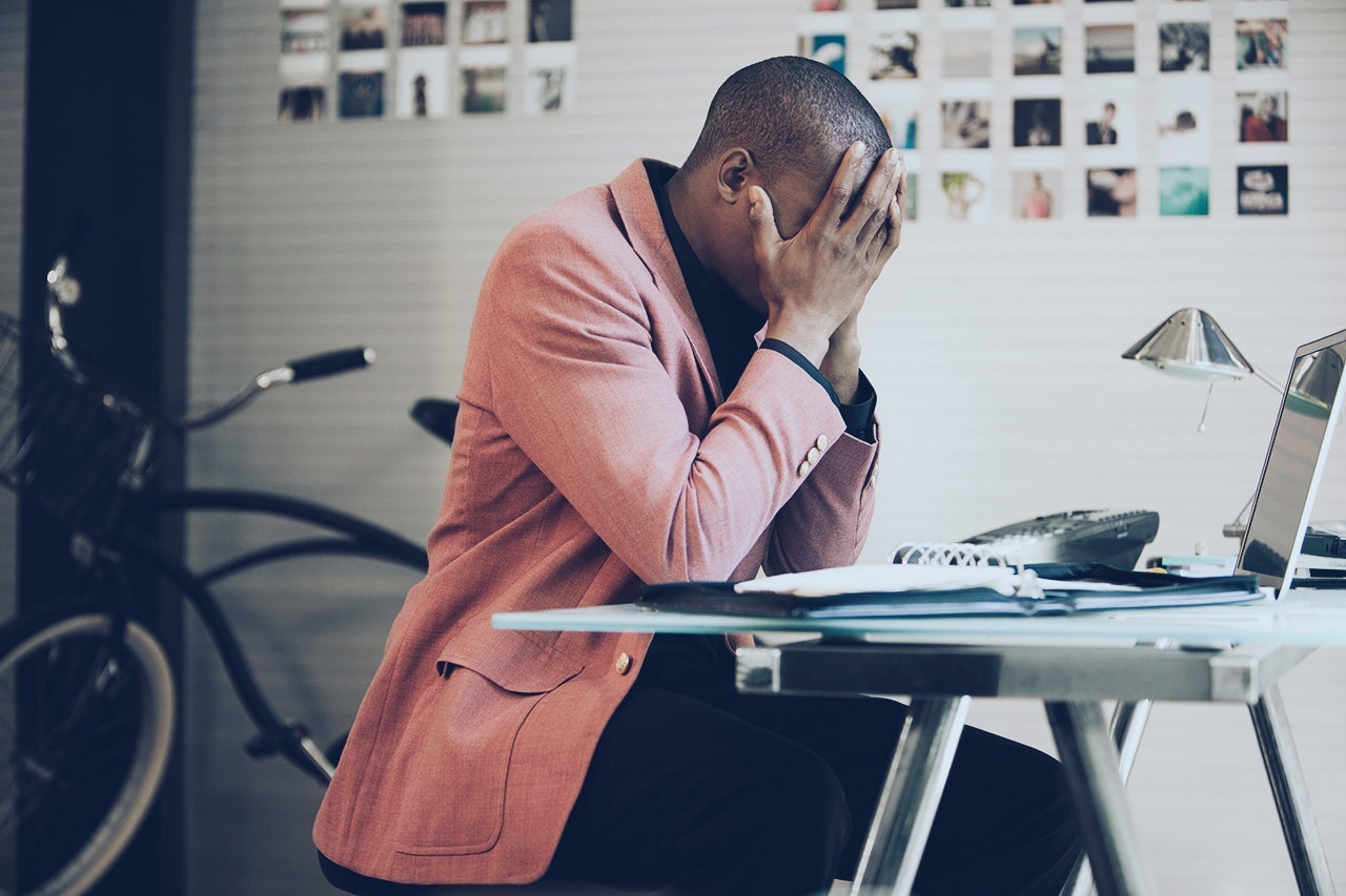 a frustrated person sits at a computer with their head in their hands