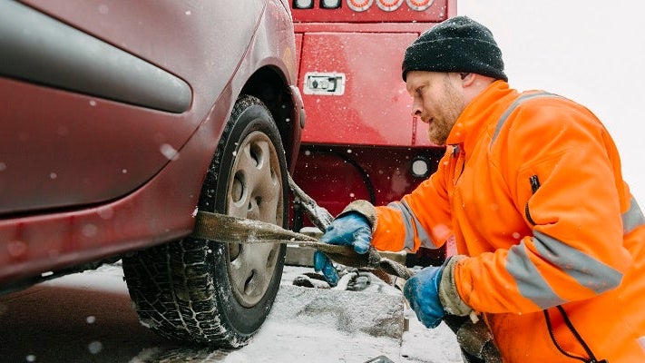 Side view of driver attaching car tire with equipment on tow truck