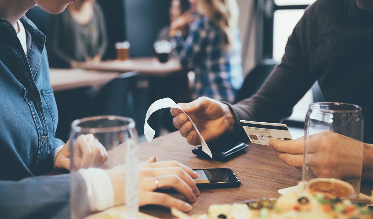Close up couple with credit card paying bill calculating tip with smart phone in brewery restaurant.