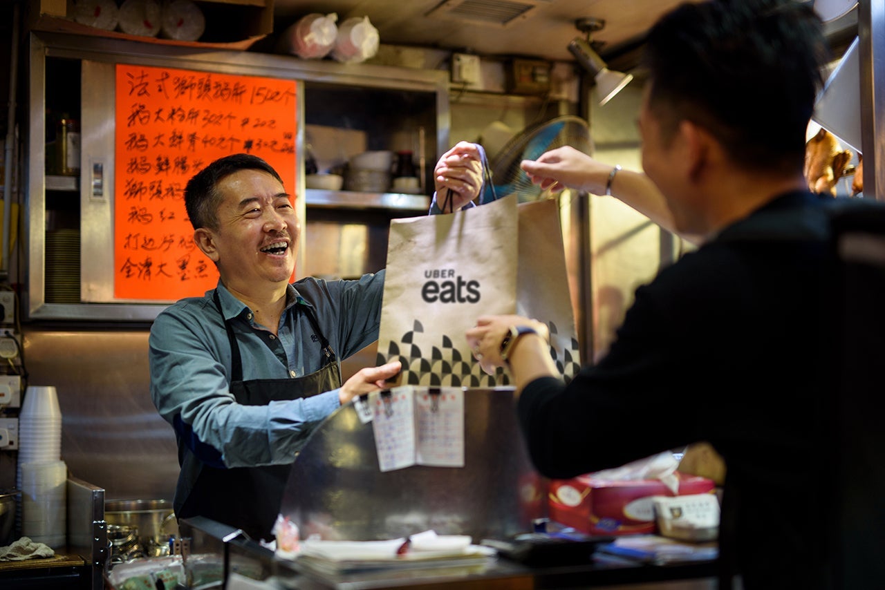 A chef hands a delivery bag full of food to a delivery driver