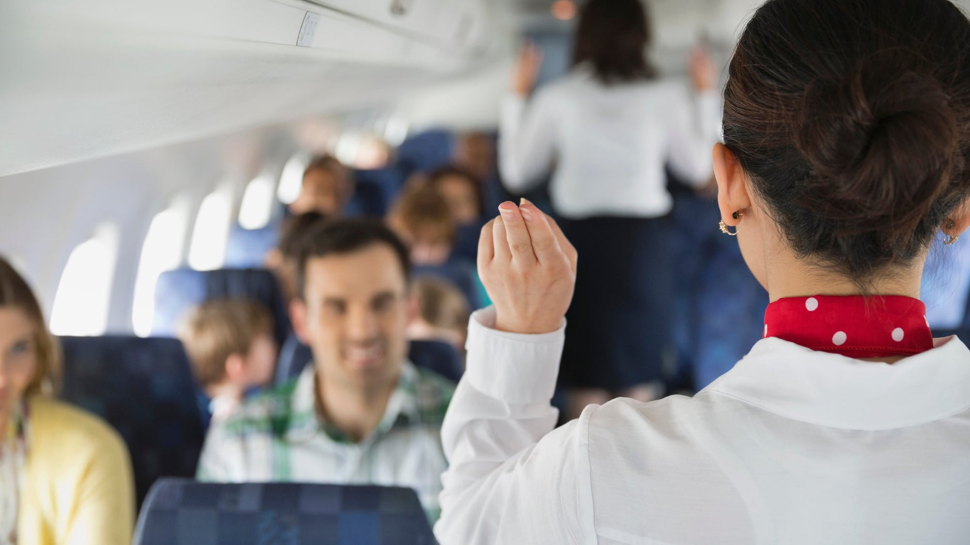 Rear view of flight attendant indicating exits to passengers in airplane