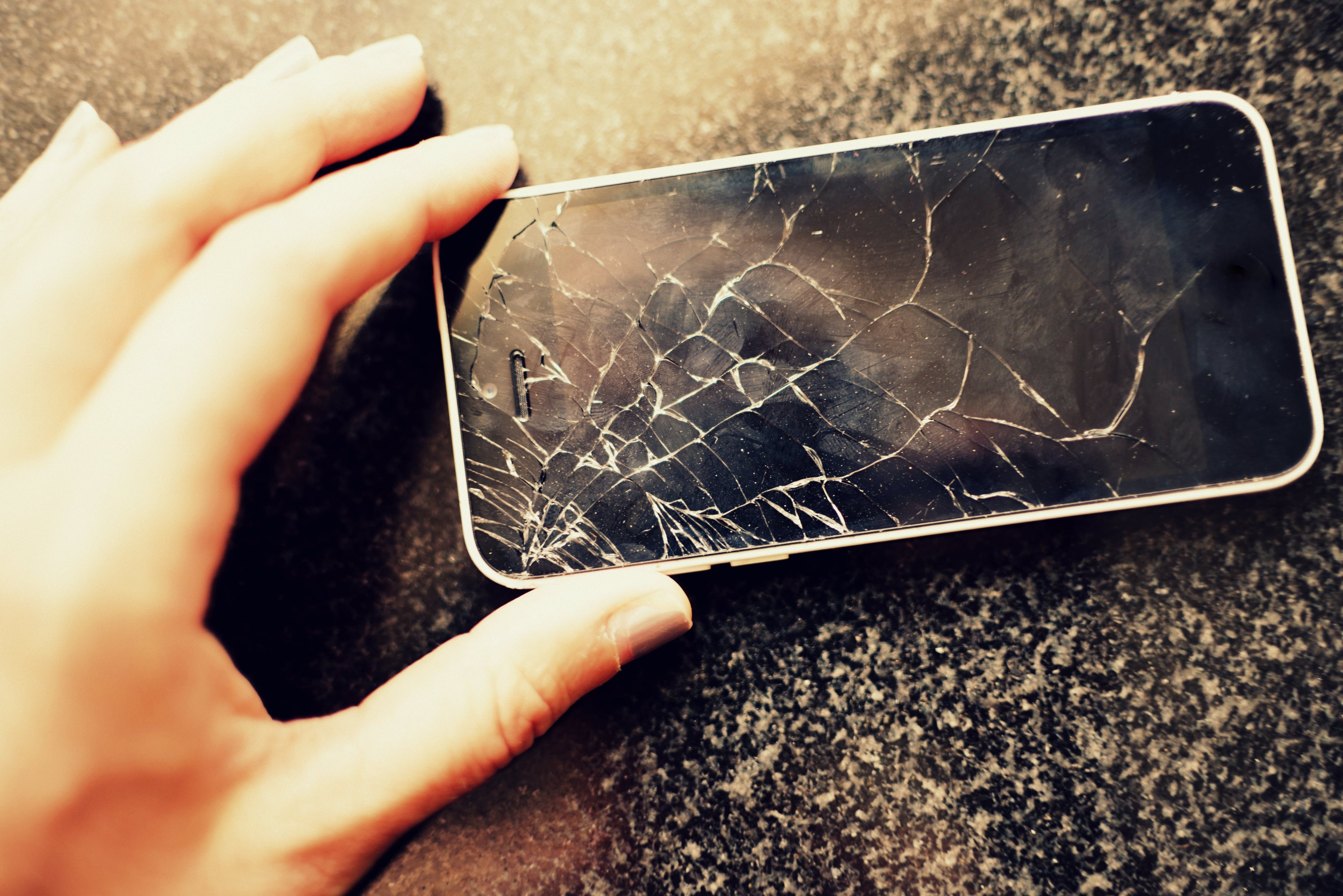 a hand holds a smart phone with a broken screen