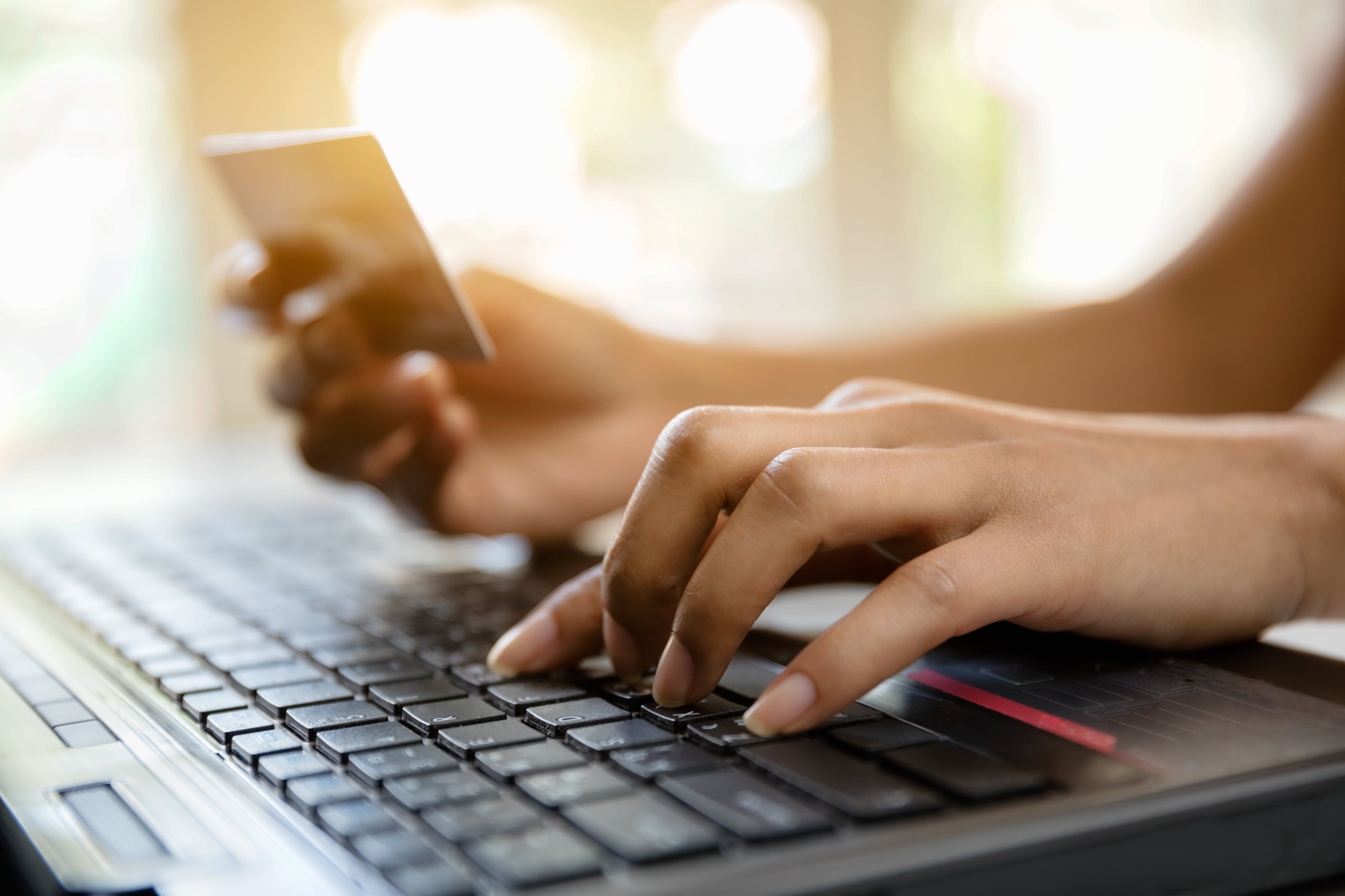 A hand holds a credit card while another hand types on a laptop