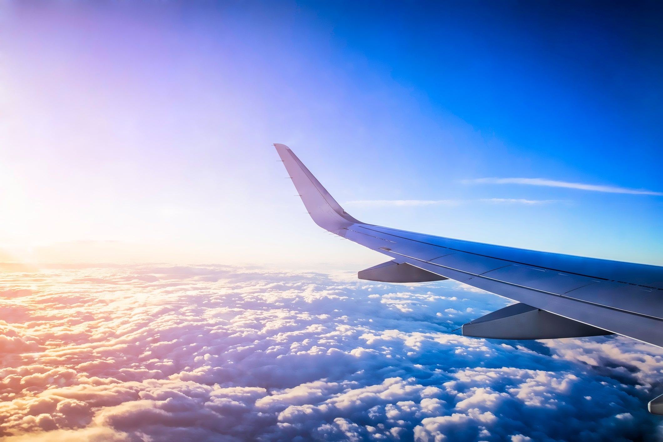 A view of the wing of a plane flying above a cloud bank.