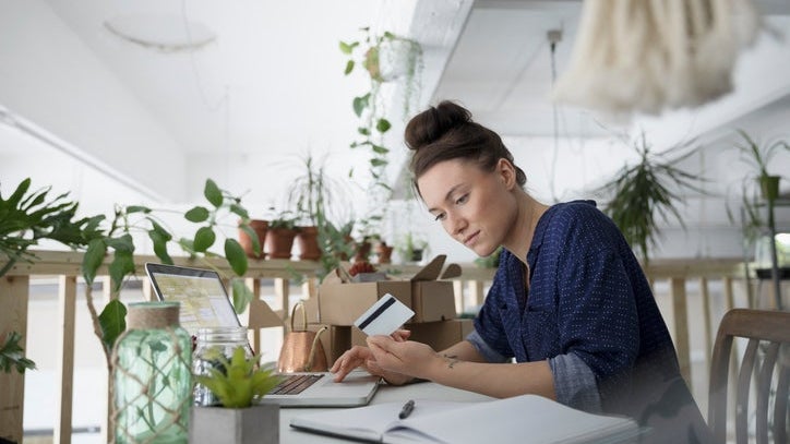 Female plant shop owner with credit card paying bills online at laptop in workshop