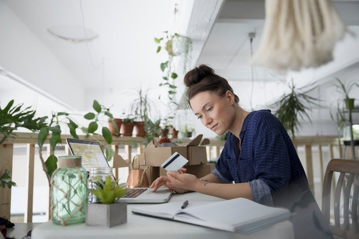 Young woman looking at a credit card while on a laptop