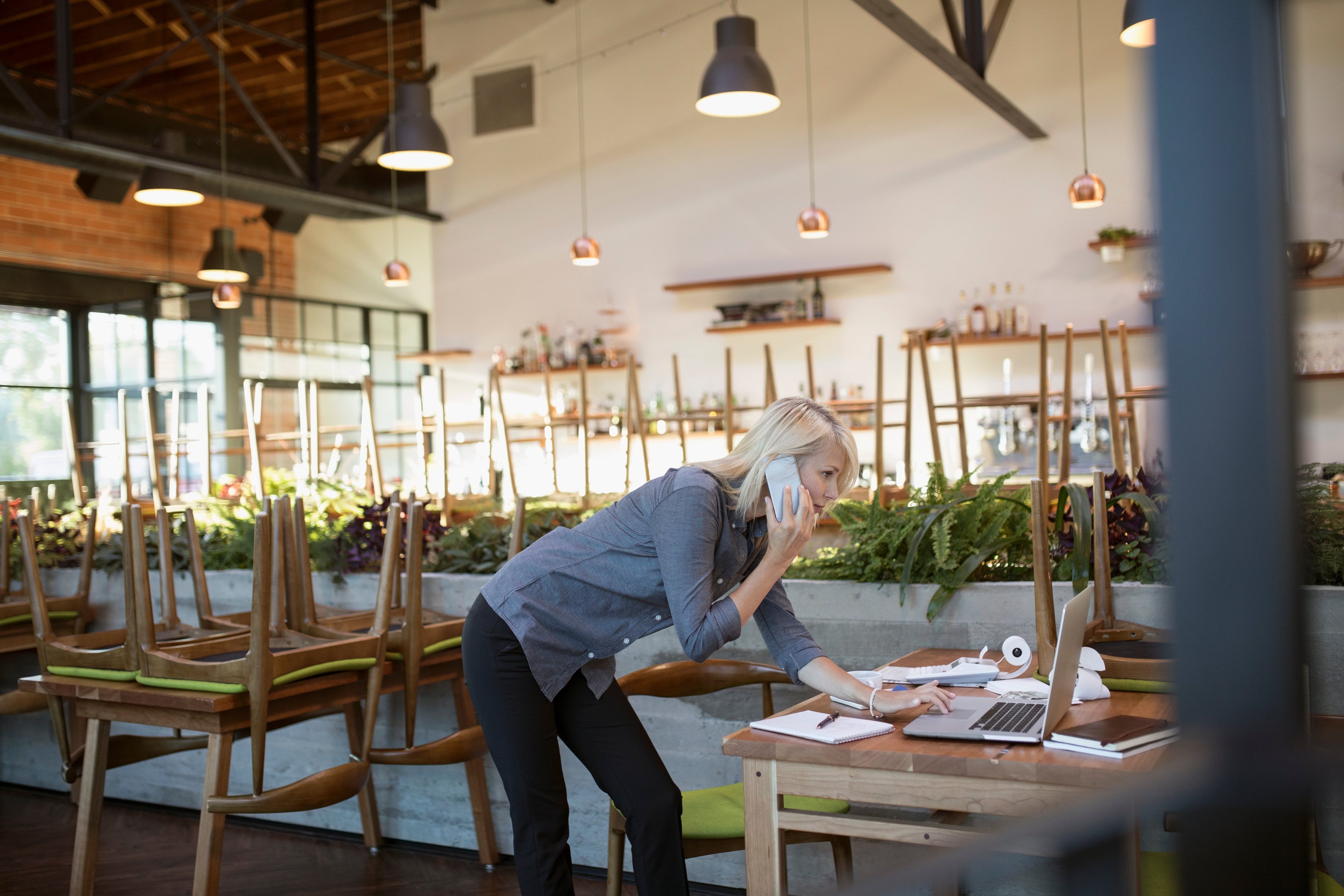 a person talks on the phone in an empty restaurant while looking at a computer