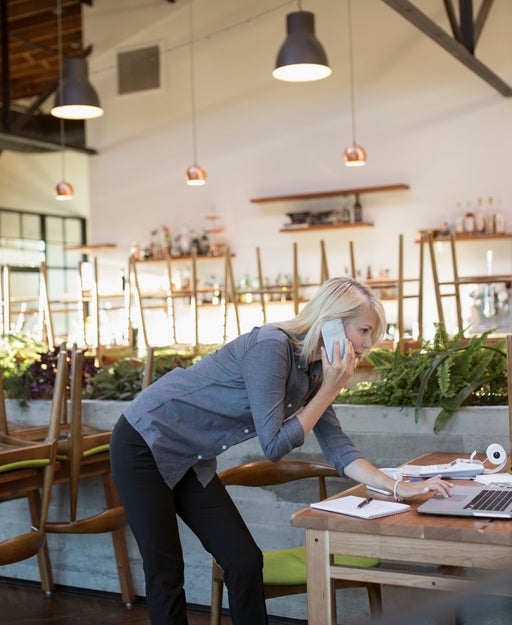 a person talks on the phone in an empty restaurant while looking at a computer