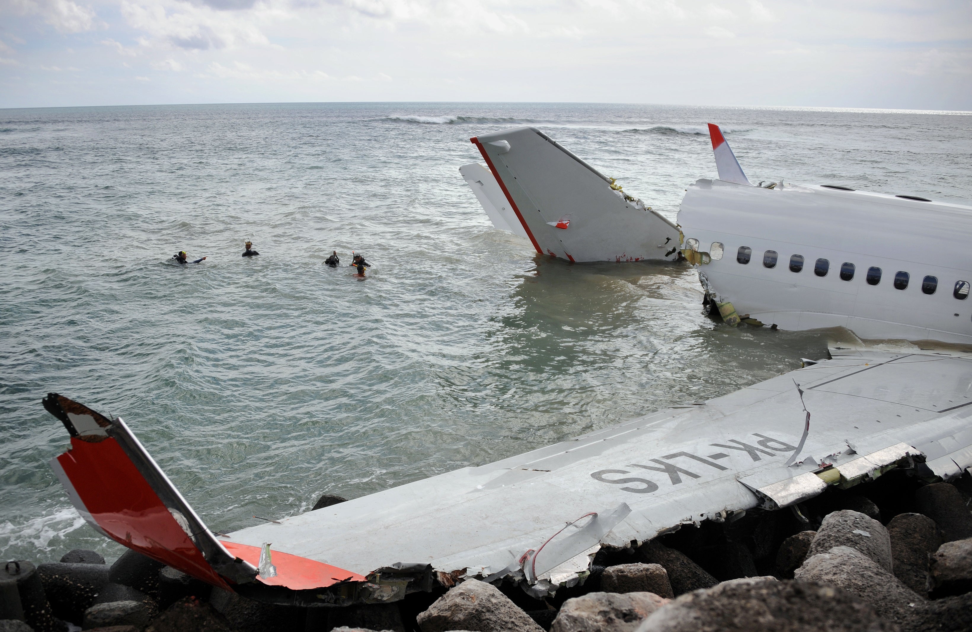 Members of a rescue team (C) prepare to dive to retrieve the black box from a Lion Air Boeing 737 (R) partially submerged in the water two days after it crashed while trying to land at Bali's international airport near Denpasar on April 15, 2013. The pilot and co-pilot of a Lion Air plane that crashed at Bali's airport have passed initial drug tests, an official said on April 15, as investigators probe the causes of the accident that left dozens injured but no fatalities. AFP PHOTO / SONNY TUMBELAKA (Photo credit should read SONNY TUMBELAKA/AFP/Getty Images)