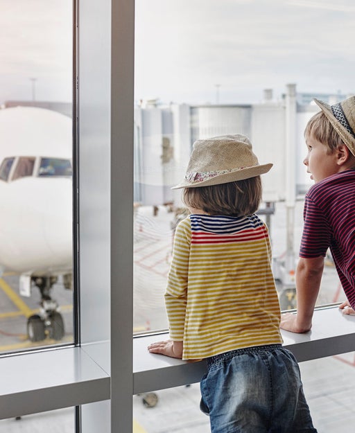 Two children wearing straw hats looking through window to airplane on the apron
