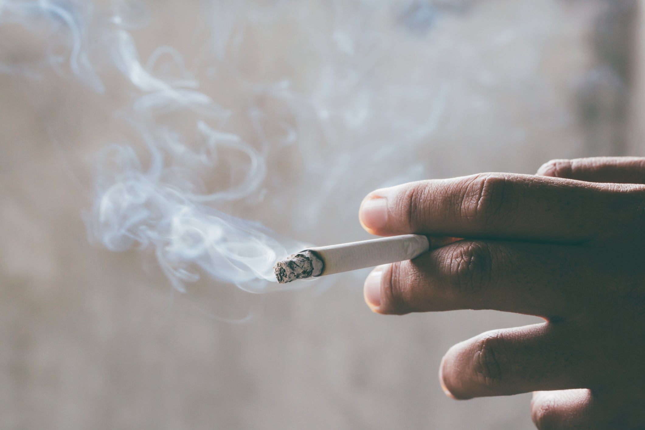 A hand holding a smoking cigarette against a blurred background