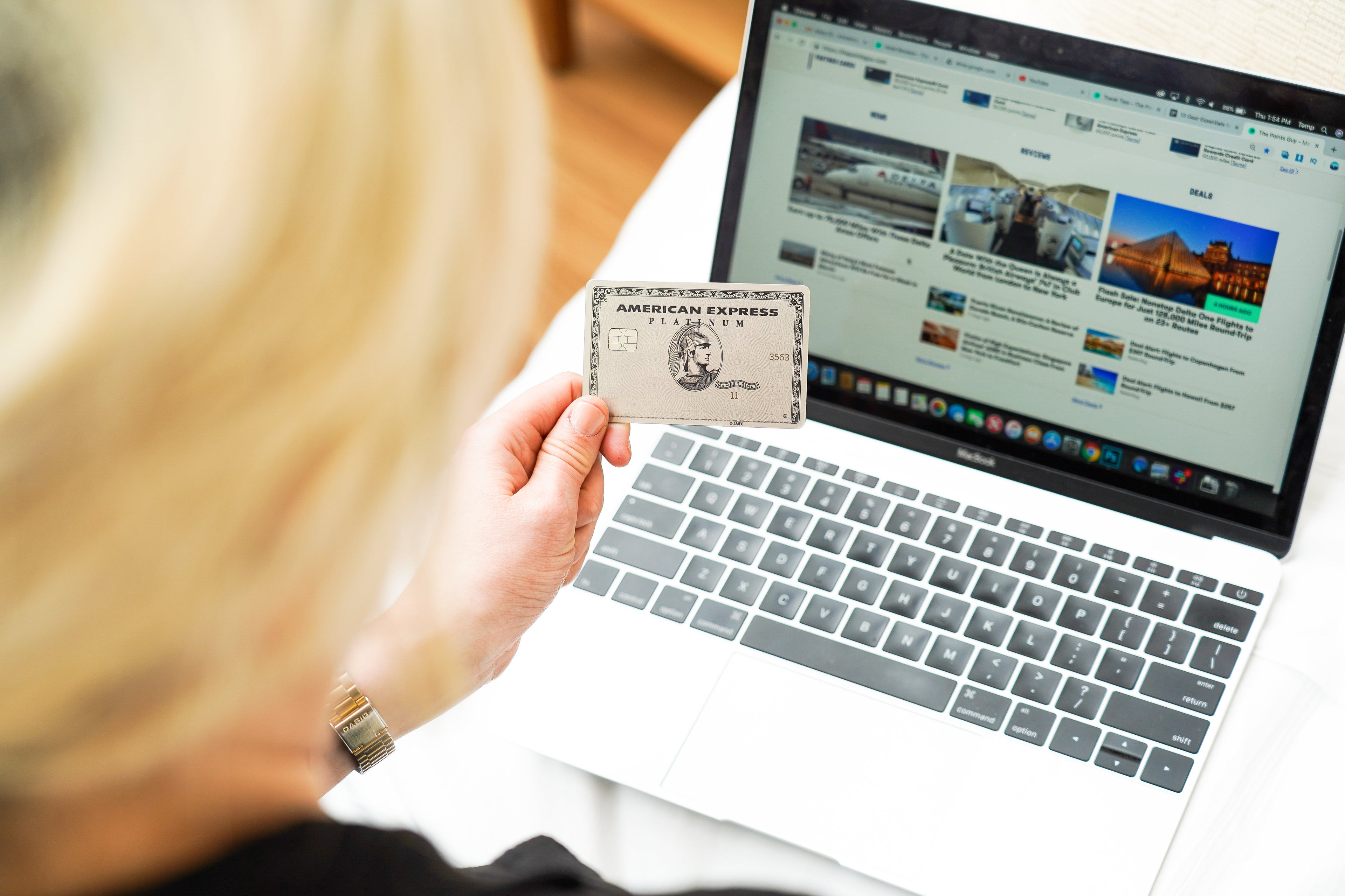 An unseen woman holds an Amex Platinum Card while looking at her computer