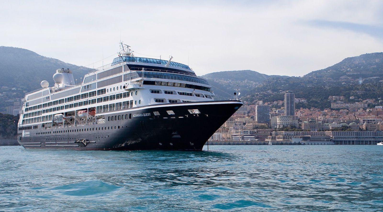 Cruise ship Azamara Quest anchored on teal-blue water with a port city in the background