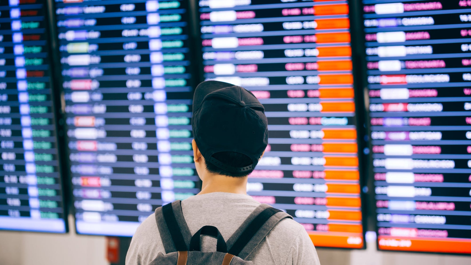 Young male traveler watching and waiting for flight time schedule on boarding time monitor screen
