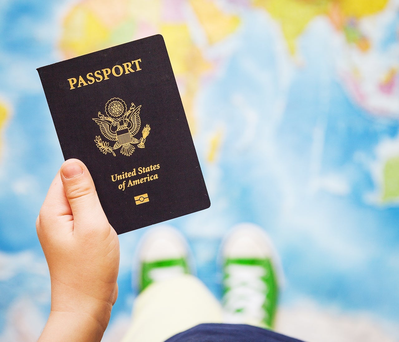 Child's hand holding US passport. Map background. Ready for traveling. Open world.