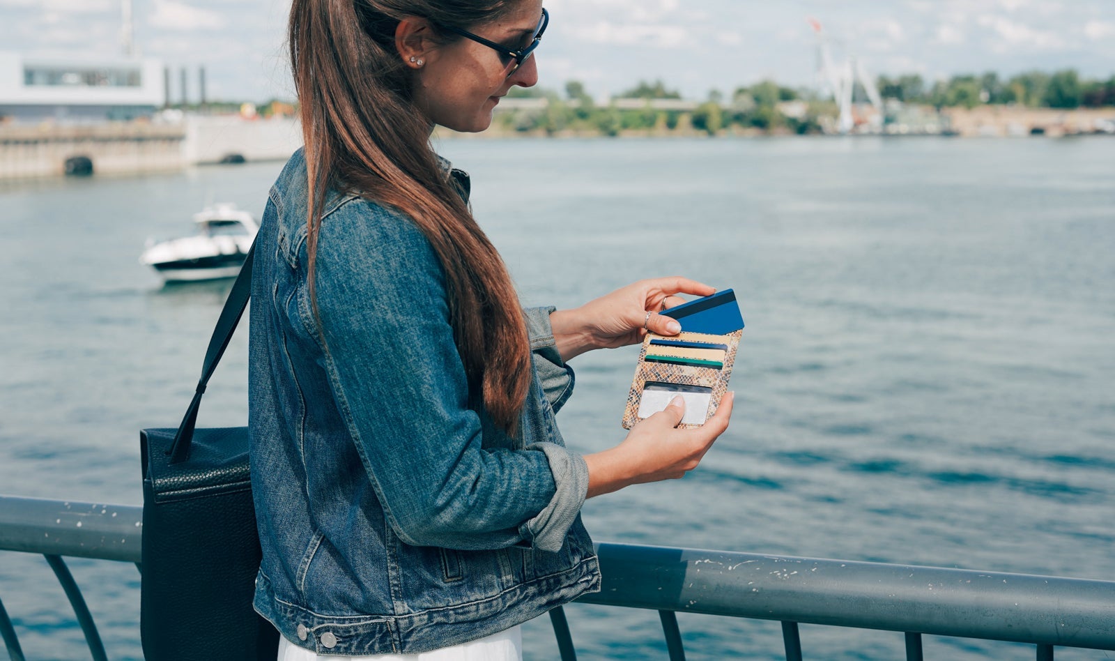 a woman stands near a lake while holding a wallet with many credit cards