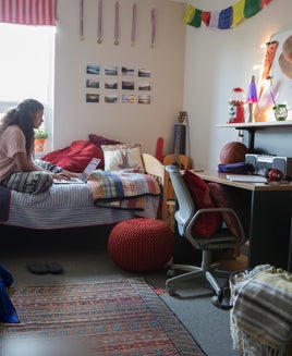 Female college student studying at laptop on bed in dorm room