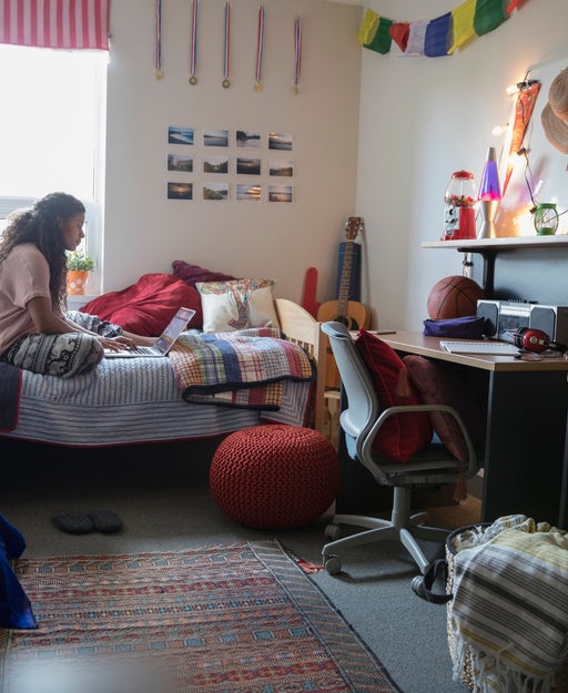 Female college student studying at laptop on bed in dorm room