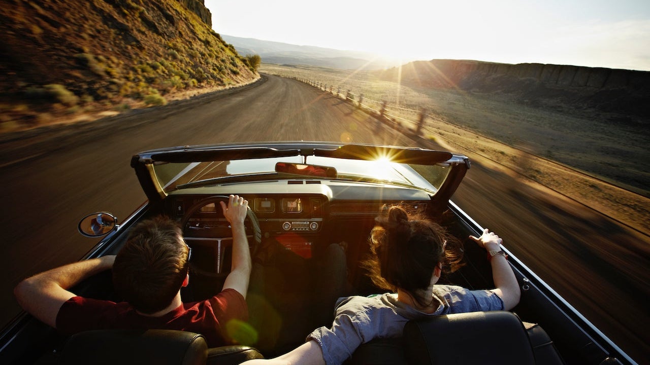 Young couple driving convertible at sunset