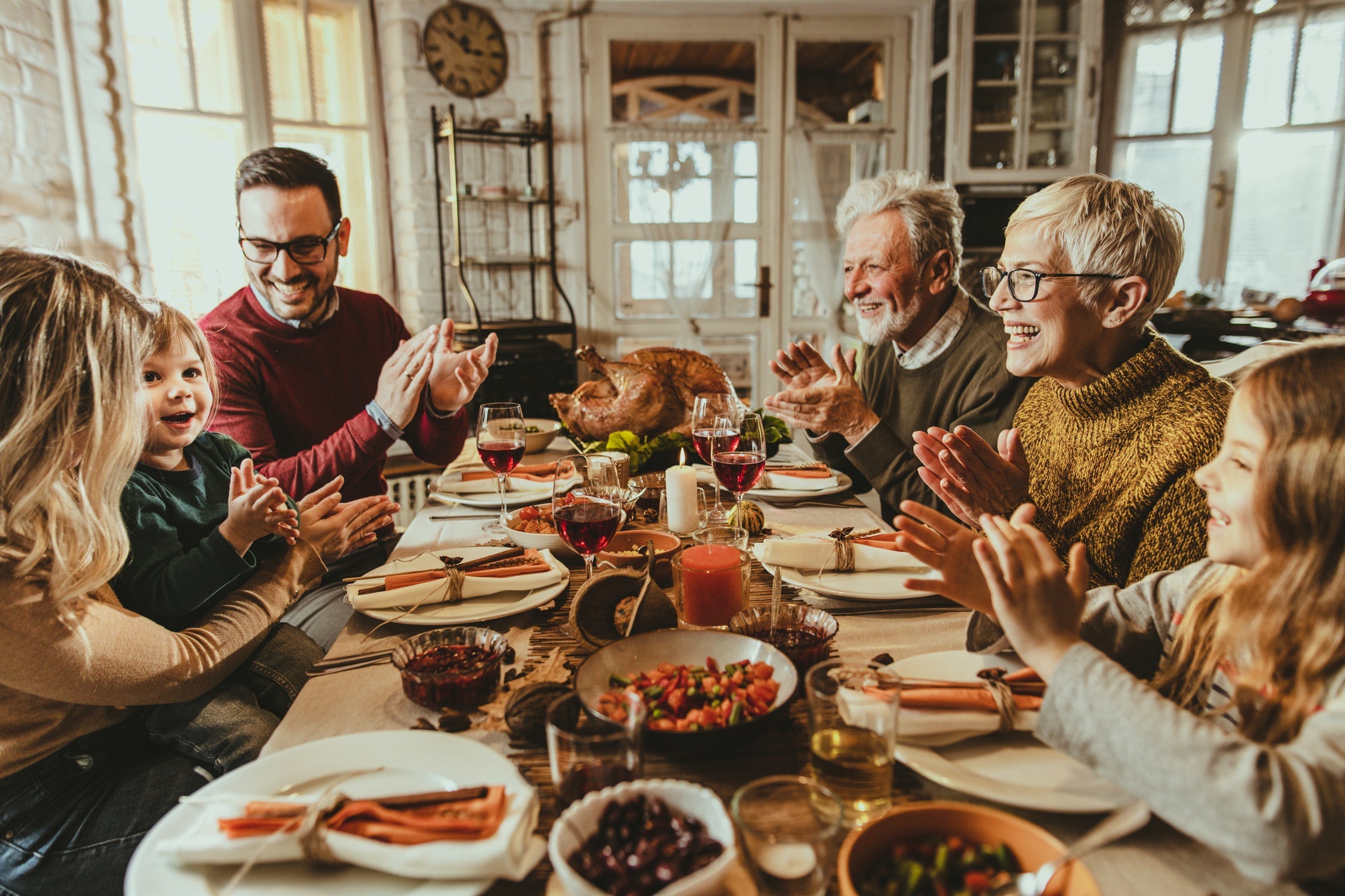 Happy extended family applauding during Thanksgiving meal at dining table.