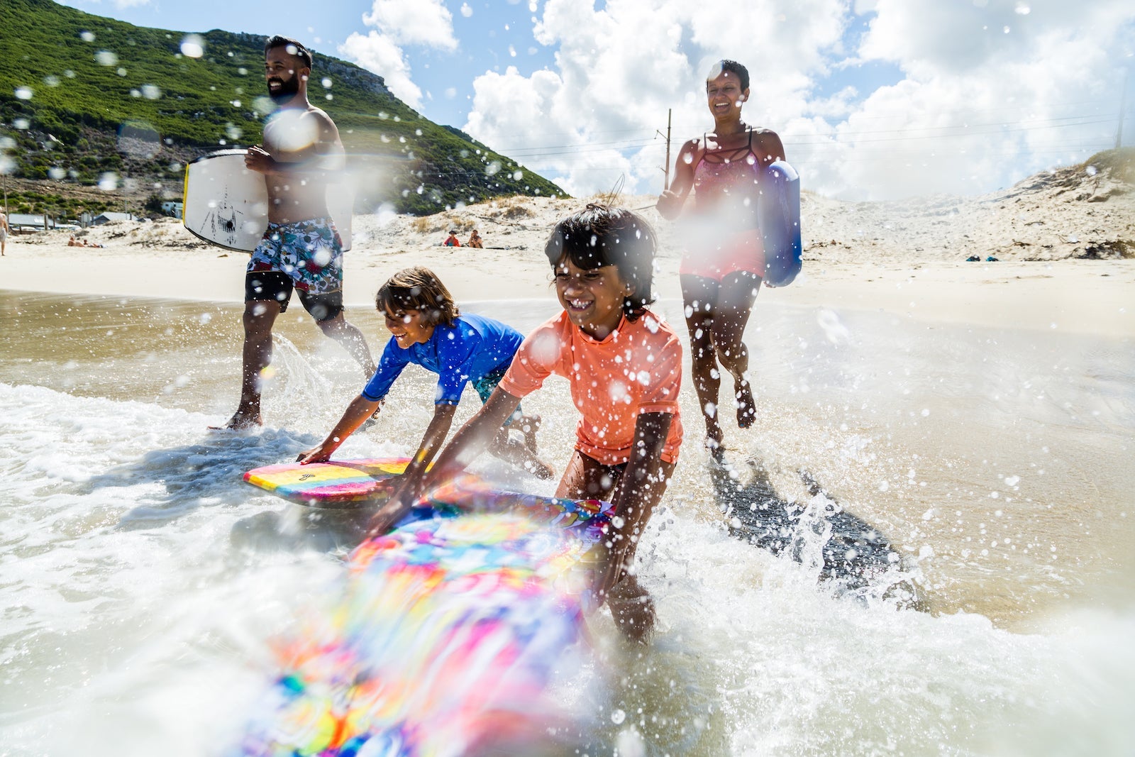 Family of four with surf boards entering the ocean from the beach.