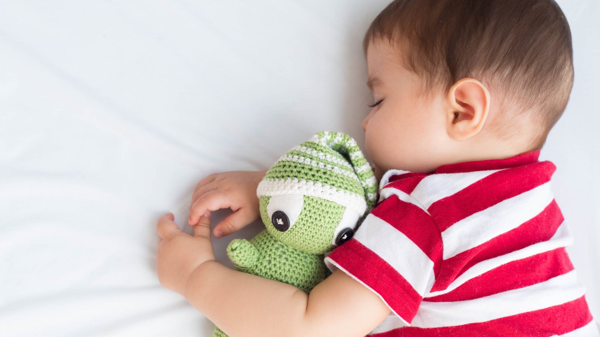 Baby sleeping in the crib with a crochet doll