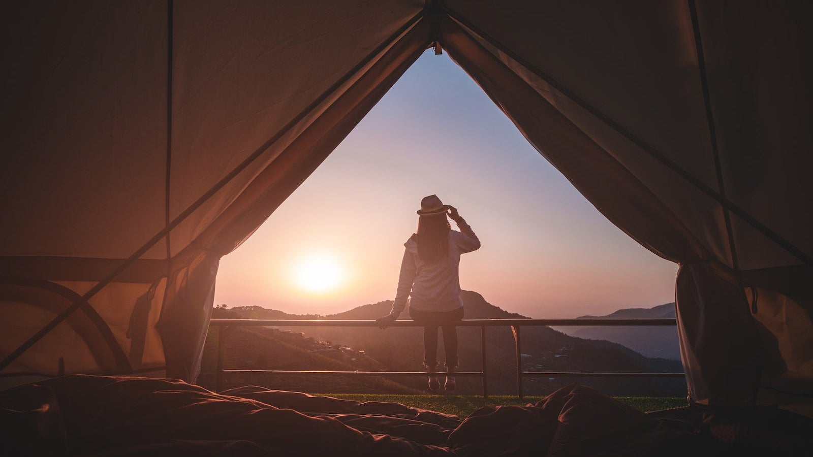 Woman traveler sitting outside camping tent and looking at sunrise view and mountain range.Travel outdoors camping for exploration and freedom concept.