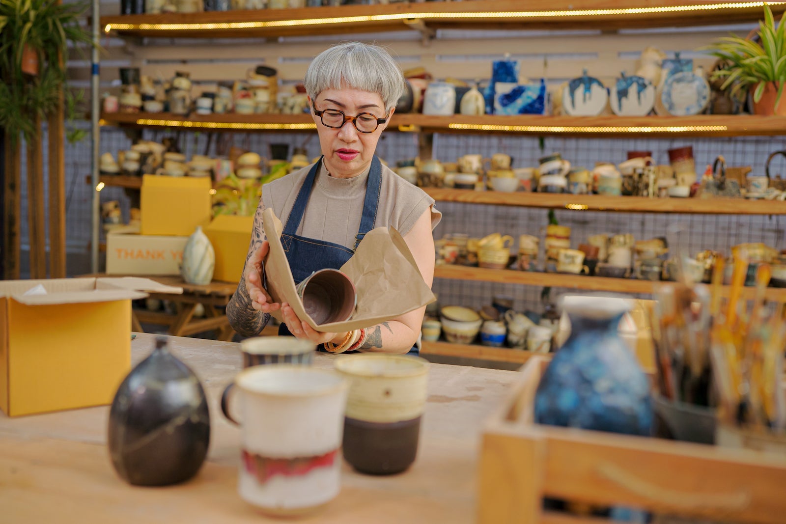 a senior packages hand-made pottery to prepare for shipping from a pottery business