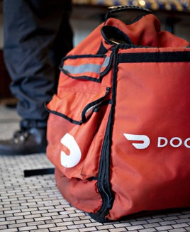 a DoorDash food delivery bag sits on the floor near an unseen person's feet