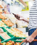 a person stands near produce in a supermarket while looking at their phone