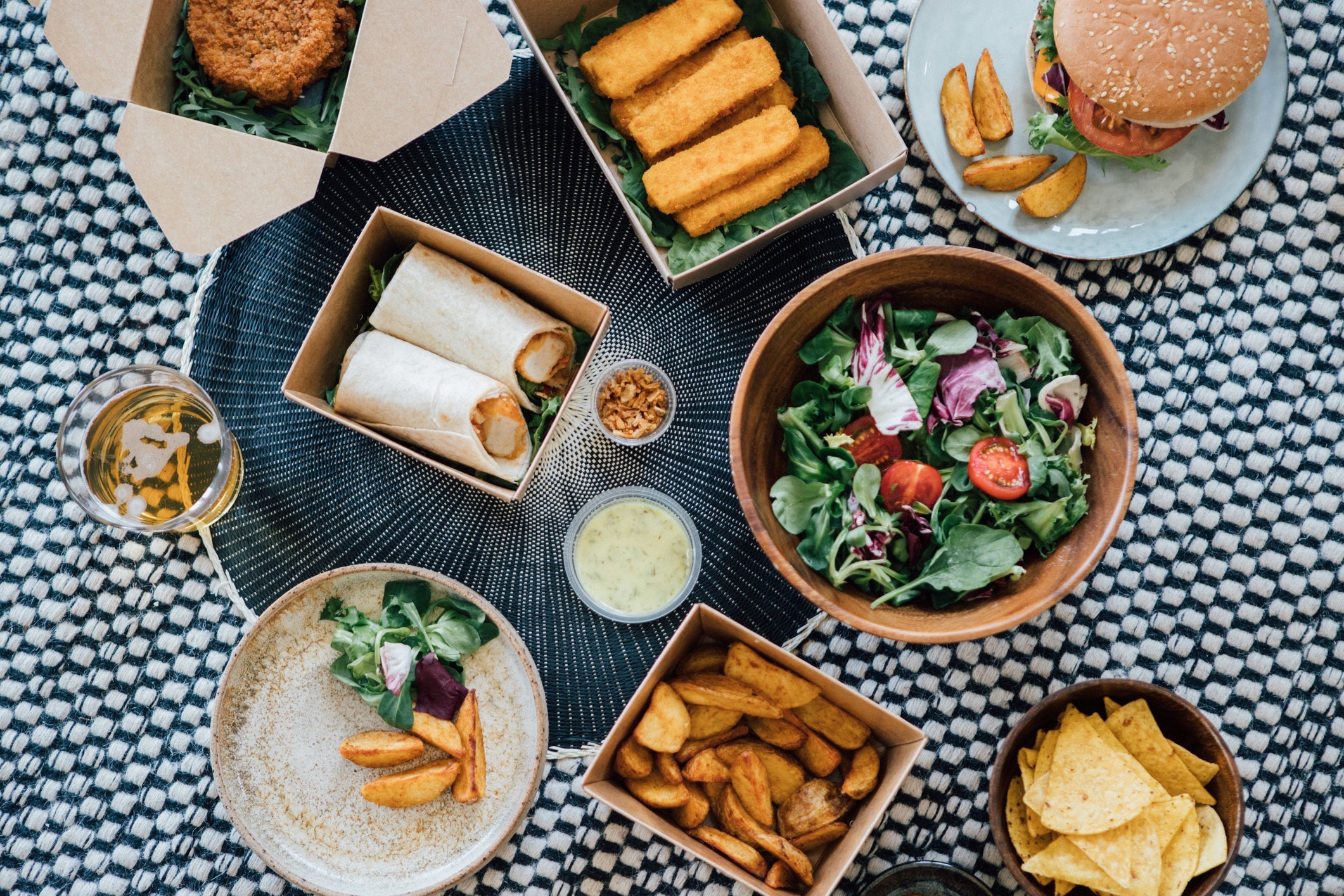 Flat lay view of delicious takeaway fast food meal - with burger, wrap sandwich, fish cake, fish sticks, potato wedges and vegetable salad