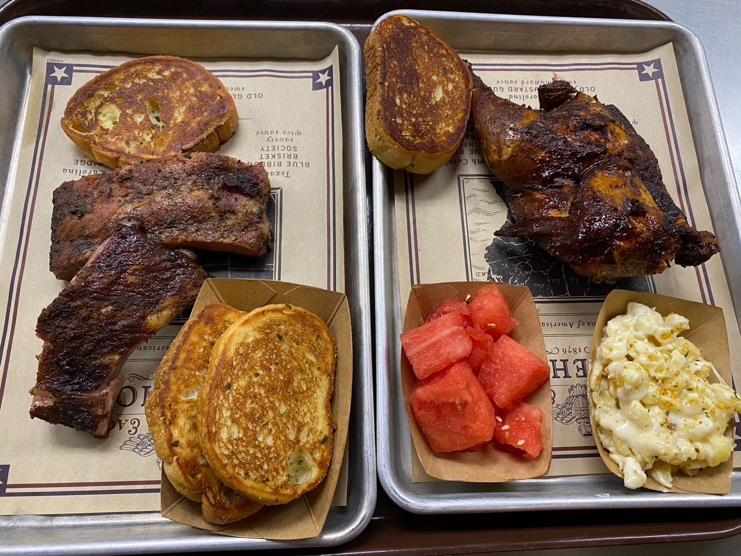 Two metal plates with barbecue chicken and ribs with toast and other side dishes at Regal Eagle Smokehouse in Epcot at Disney World