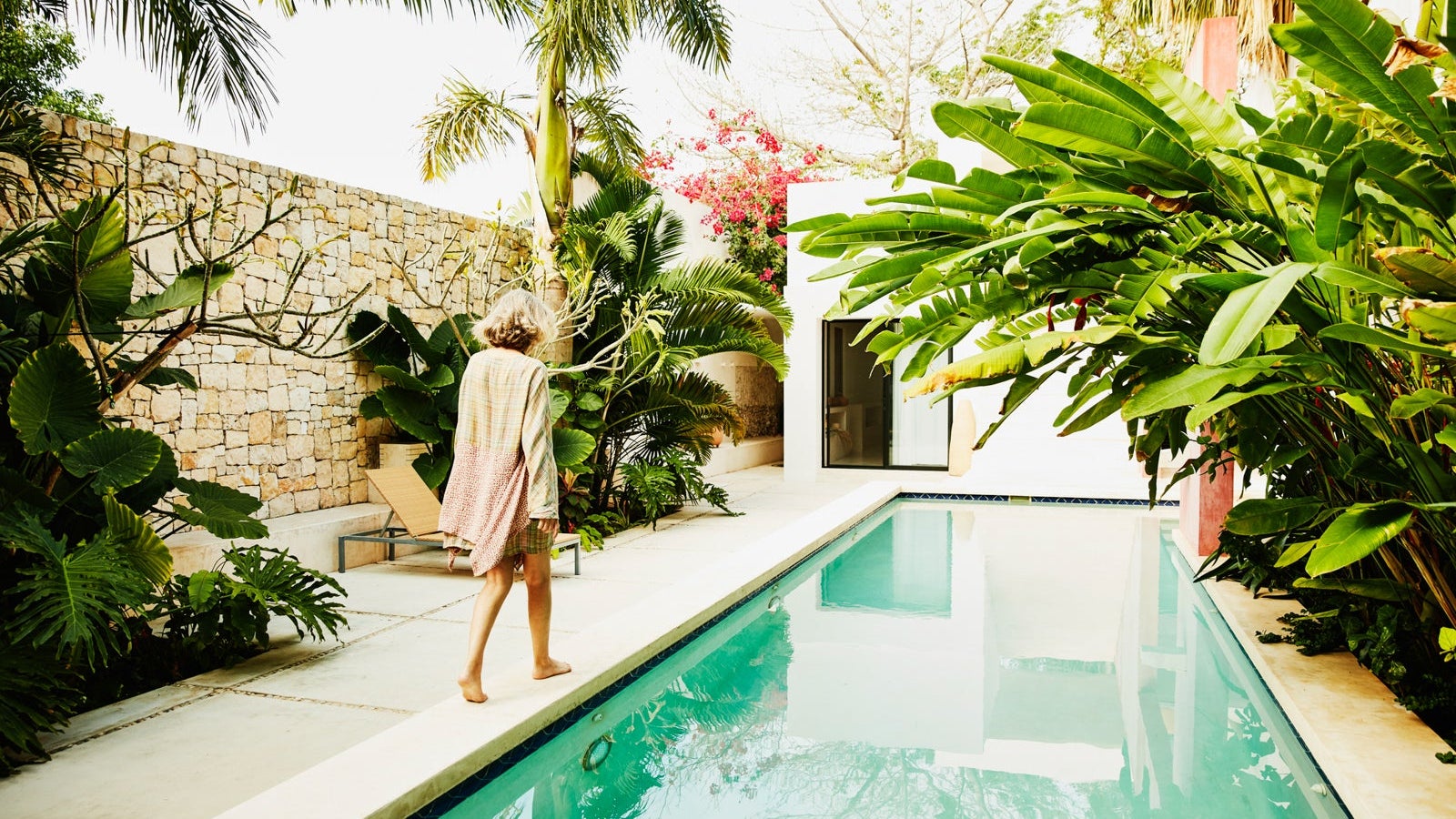 Senior woman walking along edge of pool at tropical spa