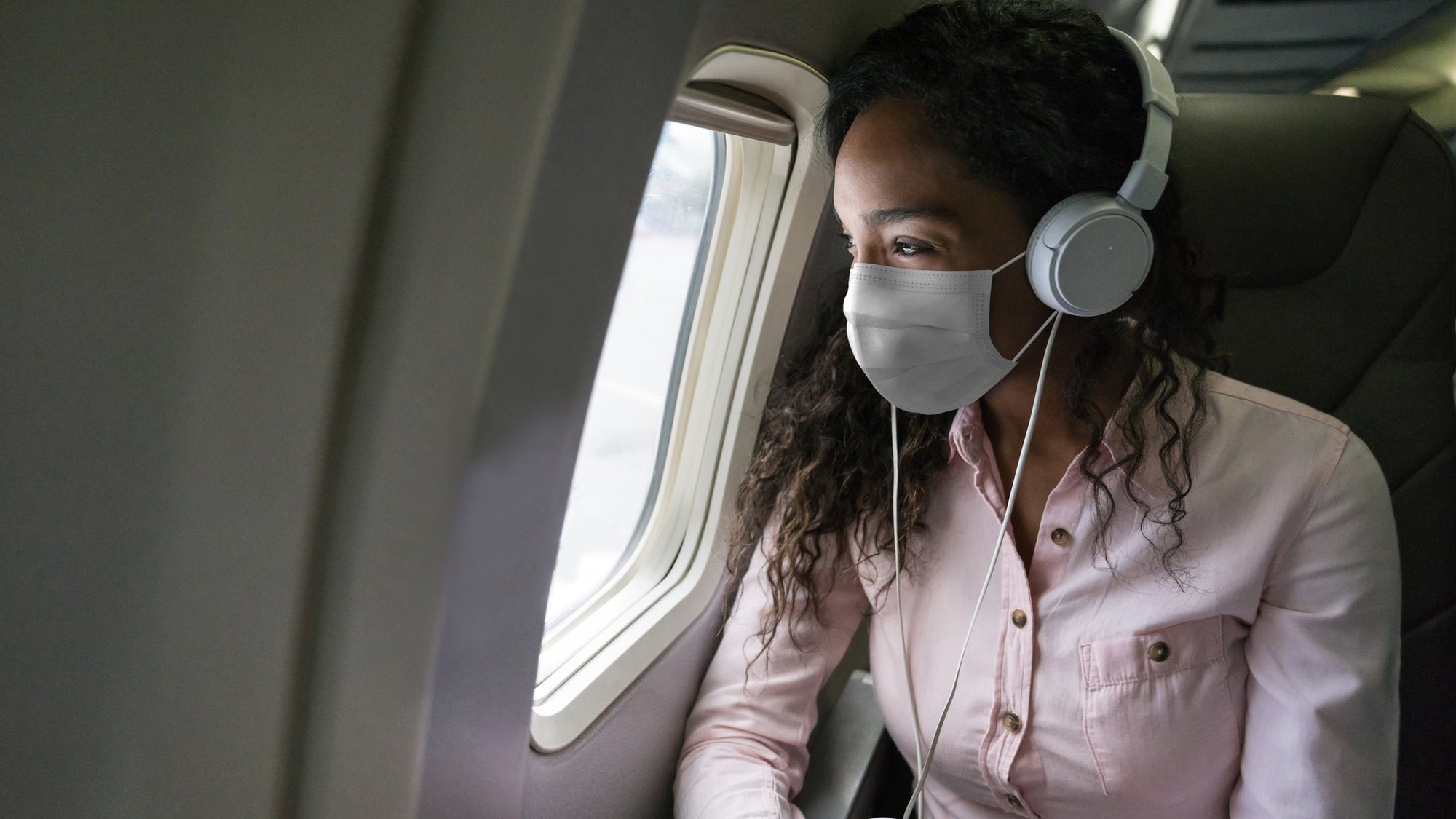 Woman listening to music while flying on an airplane wearing a facemask